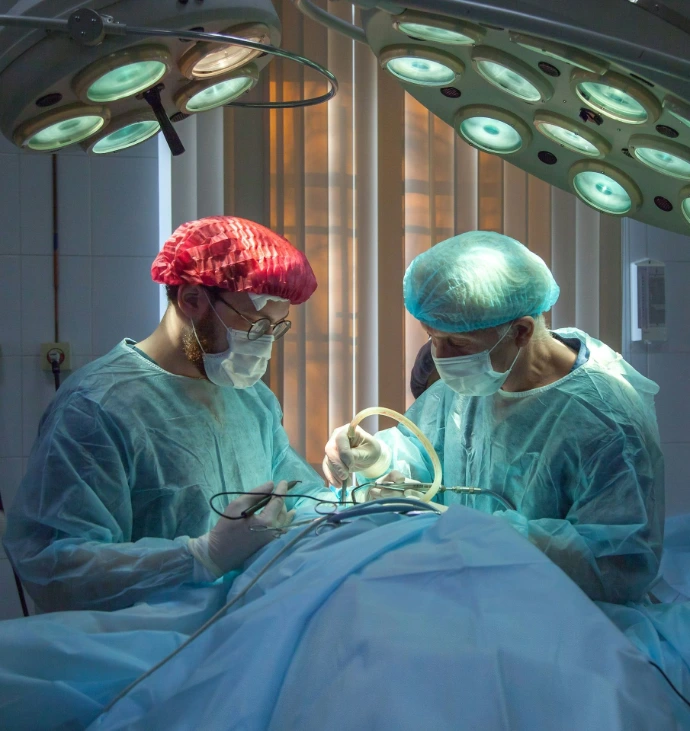 Two surgeons in blue scrubs and masks performing surgery under bright overhead lights